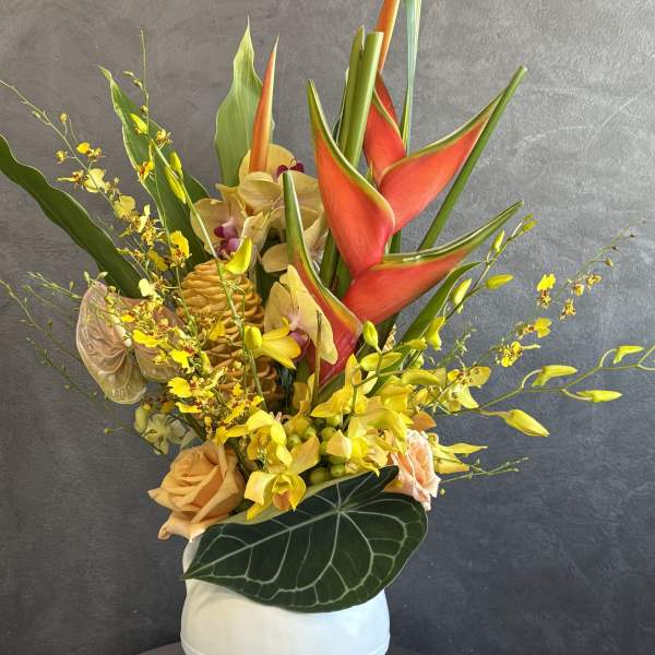 Tropical arrangement with red heliconia, yellow orchids, and peach roses in a white vase