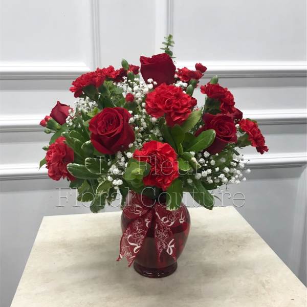 Red roses and carnations in a red glass vase with a patterned ribbon