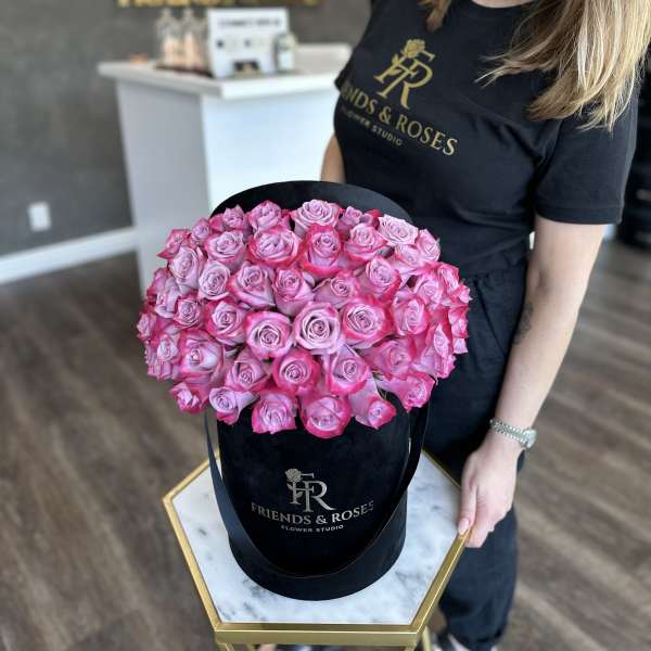Pink roses arranged in a black hatbox held by a woman