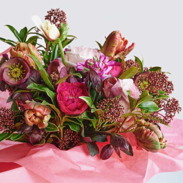 Hand-tied bouquet of pink and burgundy blooms wrapped in pink tissue paper.