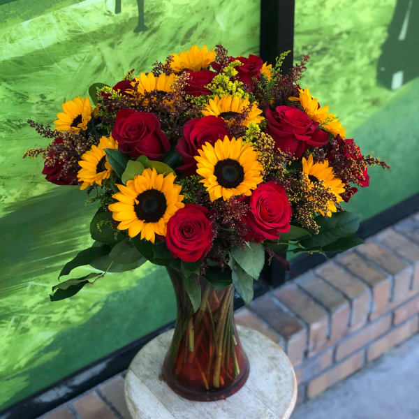 Bouquet of red roses and yellow sunflowers in a glass vase
