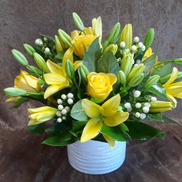 Yellow lilies and roses arranged in a white vase