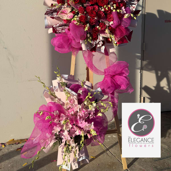 Large standing floral display of red roses and pink flowers with magenta ribbon