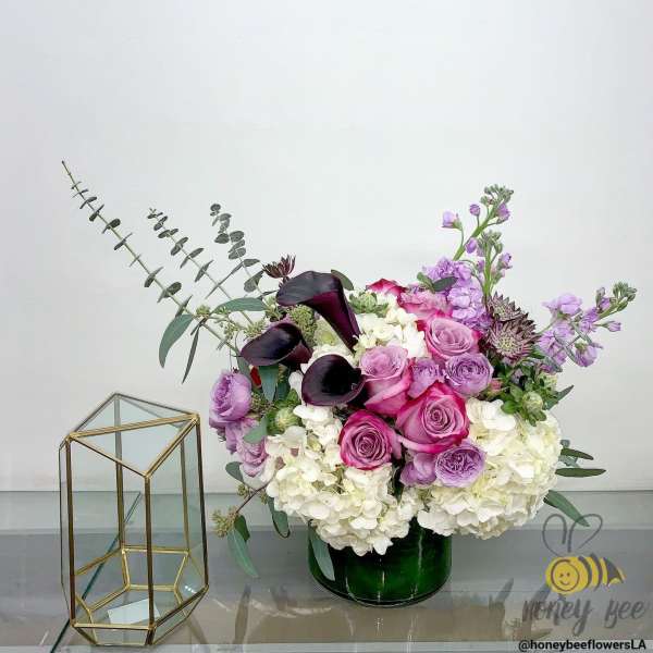 Pink and purple floral arrangement in a green vase beside a glass terrarium