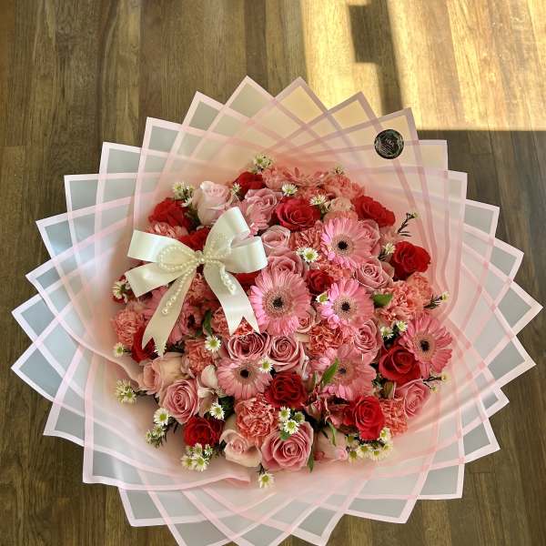 Pink and red rose bouquet with gerbera daisies and a white ribbon bow