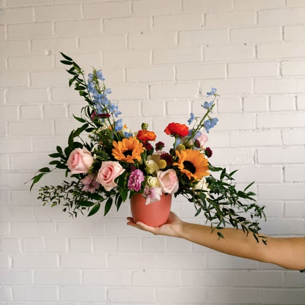 Colorful mixed bouquet in a coral vase with roses and sunflowers