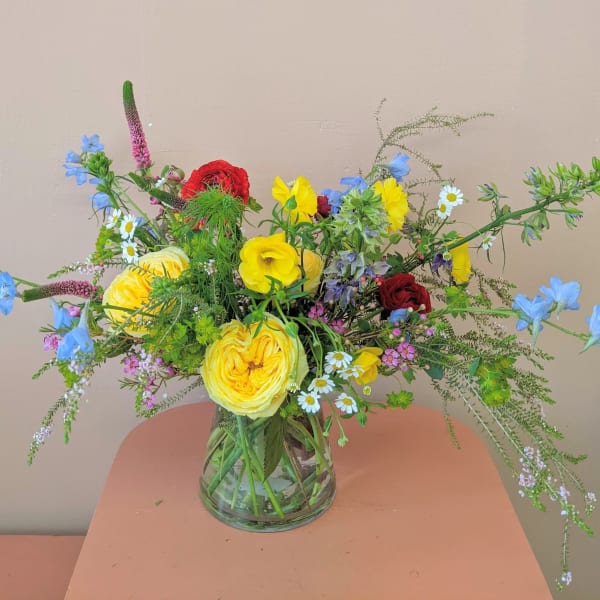 Mixed bouquet of yellow, red, and blue flowers in a clear glass vase