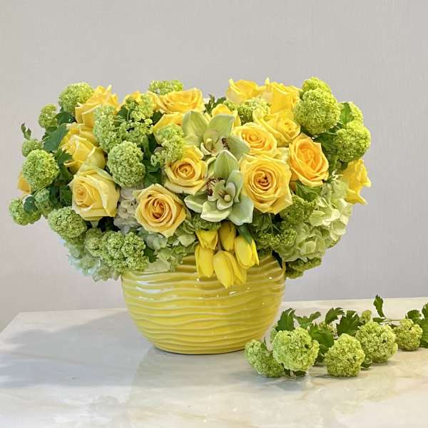 Yellow roses and green hydrangeas arranged in a yellow vase.