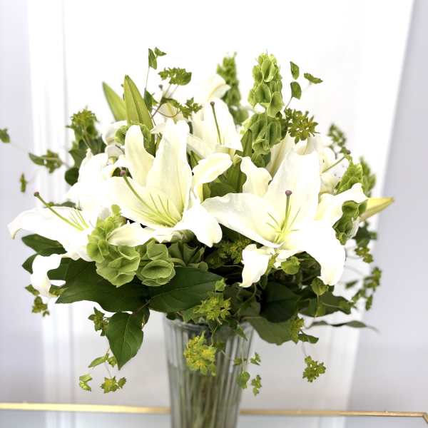 White lilies in a clear glass vase with green filler flowers