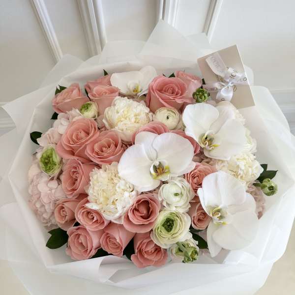 Pink rose bouquet with white orchids and cream blooms wrapped in white paper