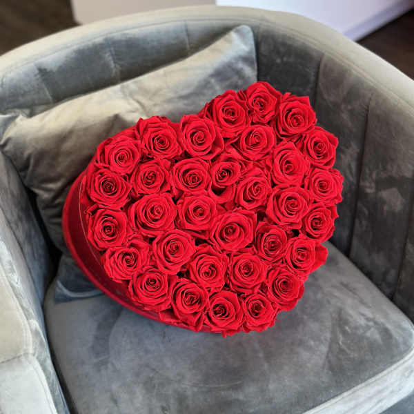 Heart-shaped box filled with red roses on a gray chair