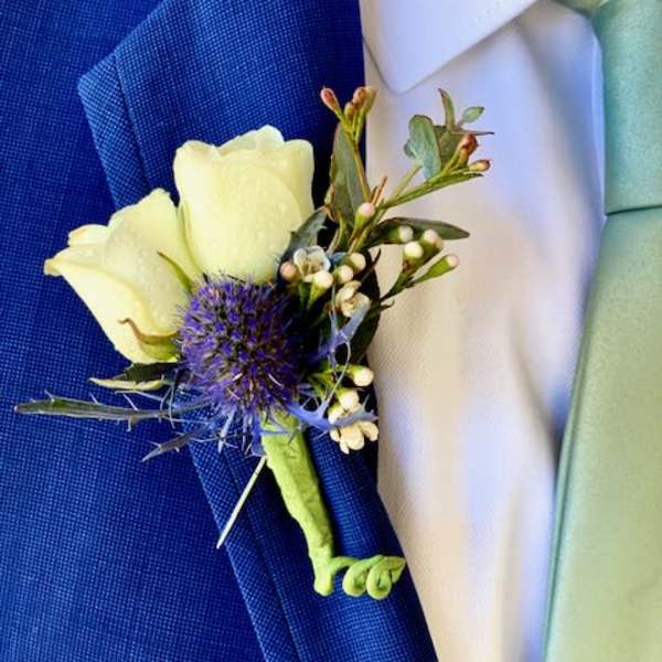White boutonniere with a purple thistle bloom on a blue suit lapel