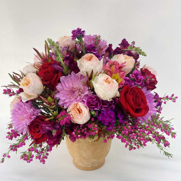 Mixed bouquet of red, pink, and peach flowers in a tan vase
