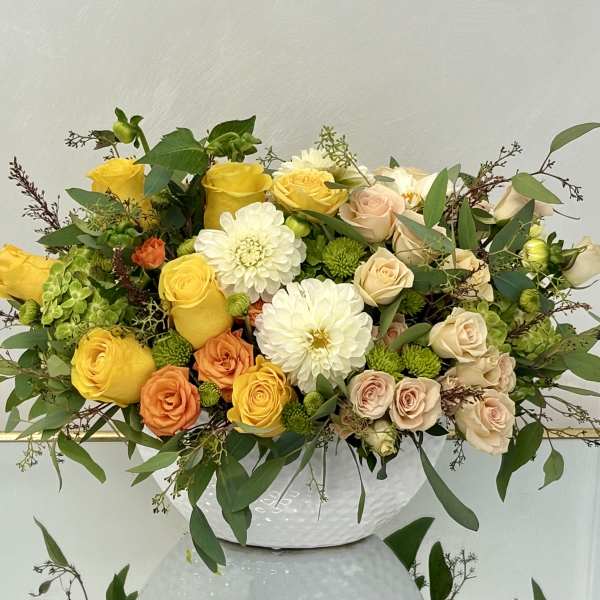 Mixed bouquet of yellow, peach, and white flowers in a white vase
