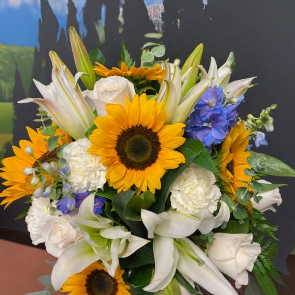 Bouquet of sunflowers, white lilies, and blue flowers in a vase