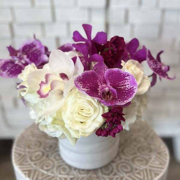 White roses and purple orchids arranged in a white vase