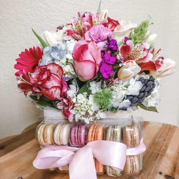 Mixed pink and white flower bouquet above a box of macarons with a pink ribbon