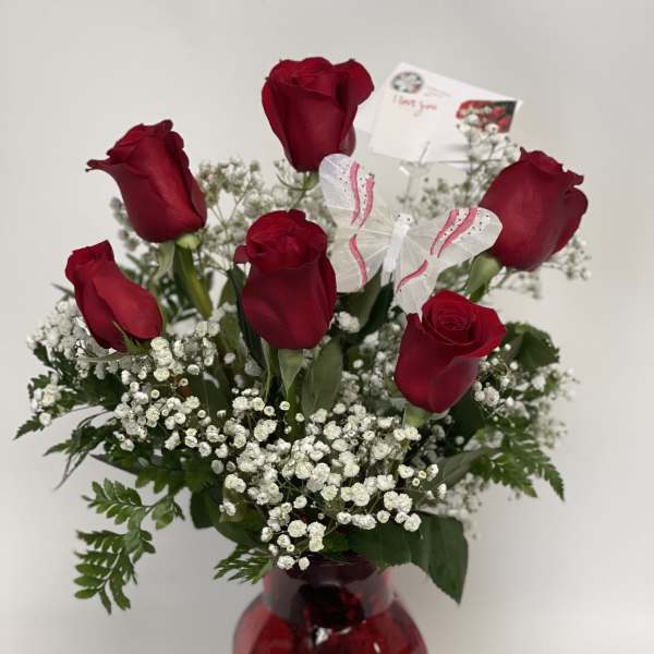 Red roses in a red glass vase with baby's breath and a butterfly decoration