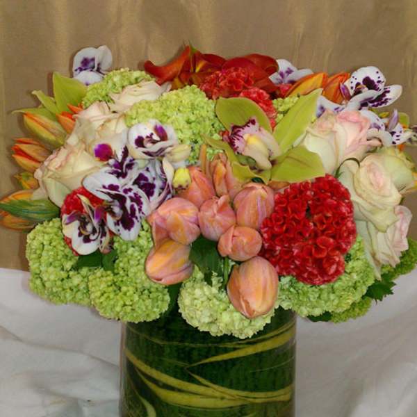 Mixed bouquet in a glass vase with orchids, roses, tulips, and green hydrangeas
