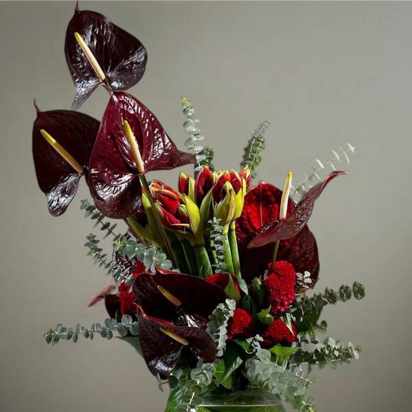 Dark red anthuriums and red flowers in a glass vase with eucalyptus