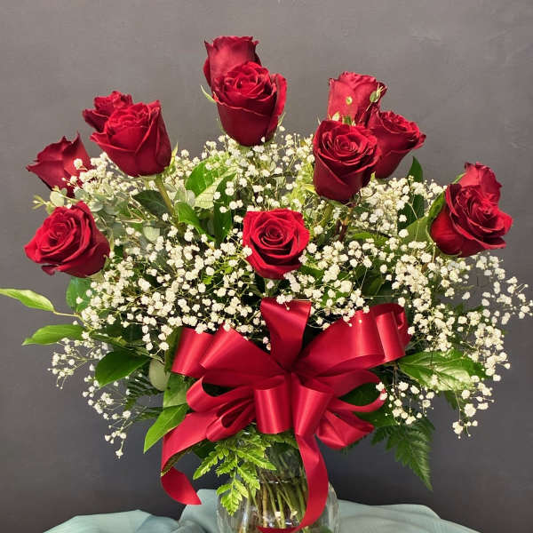 Red roses and baby's breath in a glass vase with a red ribbon