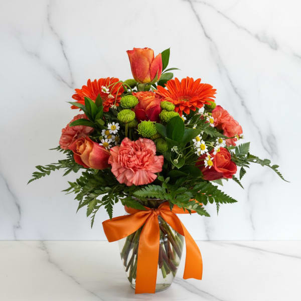 Orange and coral bouquet in a glass vase with a ribbon