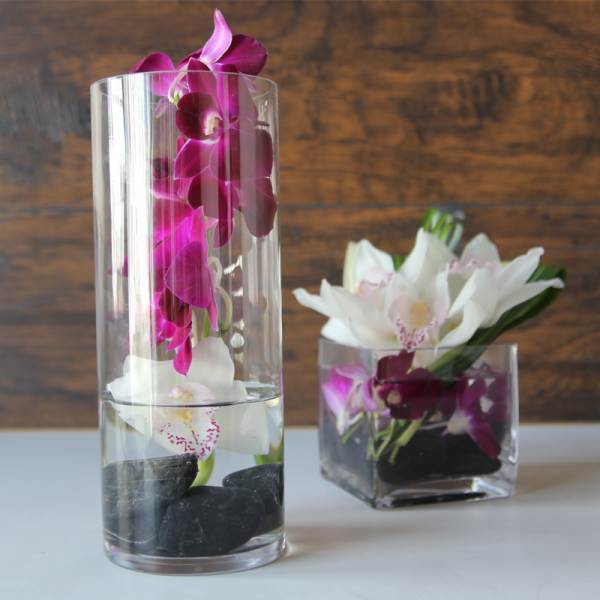 White and magenta orchids arranged in glass vases with black stones