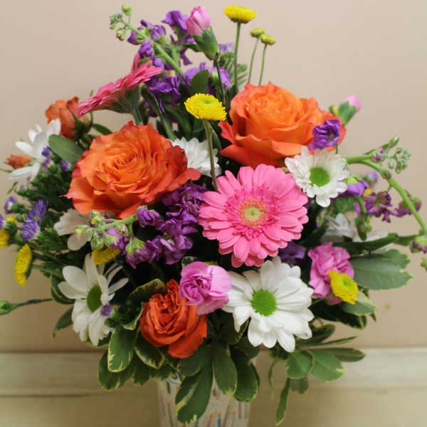 Mixed bouquet of orange roses, pink gerbera daisies, and white daisies in a patterned vase