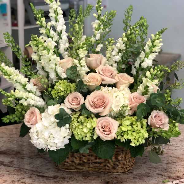 Basket arrangement of pale pink roses and white snapdragons with hydrangeas