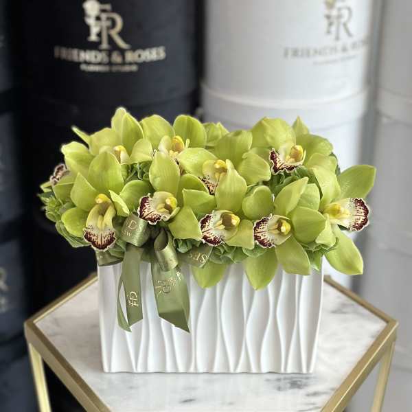 Green orchid arrangement in a white rectangular vase with ribbon