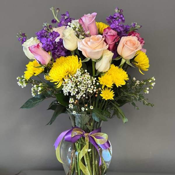 Mixed bouquet of roses and yellow chrysanthemums in a glass vase with ribbon