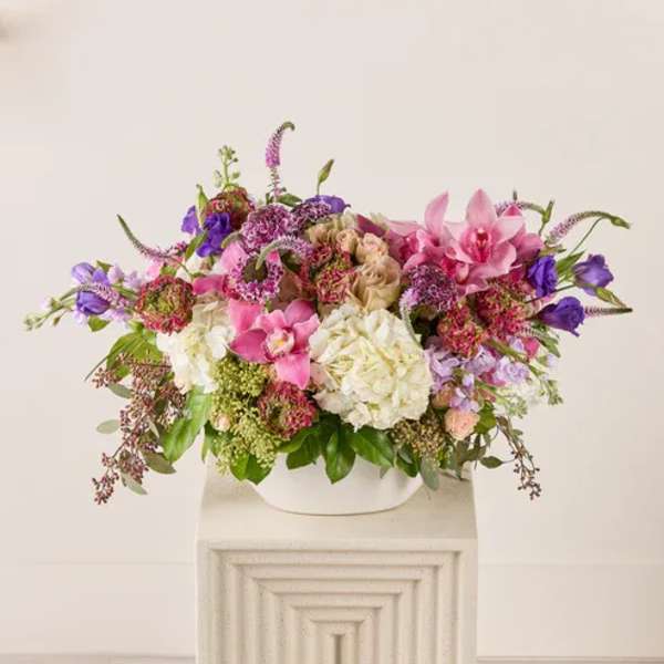 Large mixed bouquet in a white container with pink, purple, and white blooms