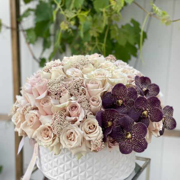 Round bouquet of pale roses and purple orchids in a white textured box