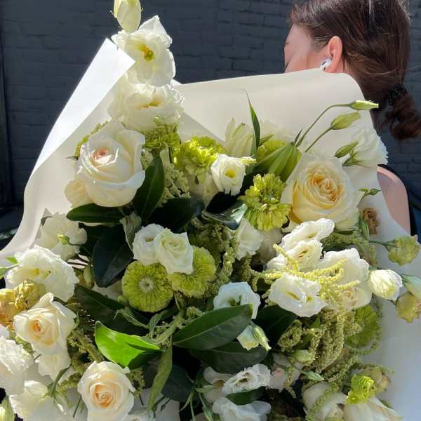 Large bouquet of white and pale green flowers wrapped in white paper