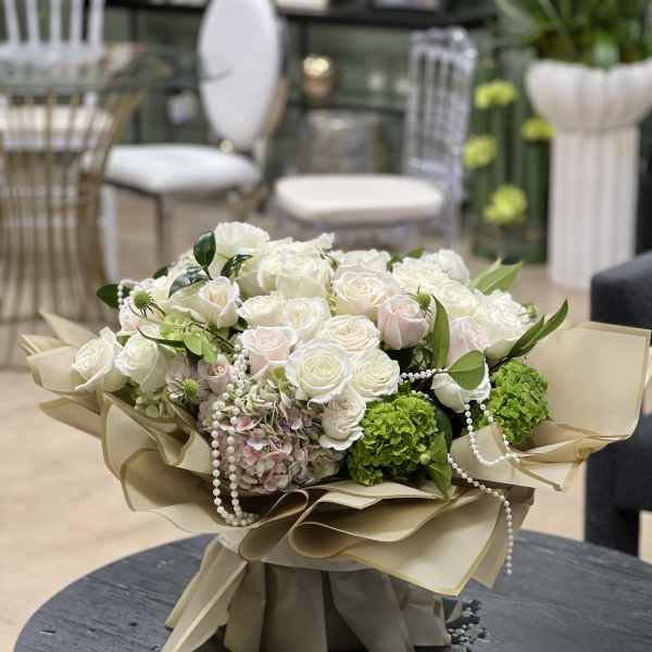 Bouquet of white roses and green hydrangeas with pearl strands in beige wrap