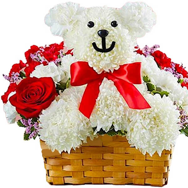 White teddy bear in a basket surrounded by red and white flowers