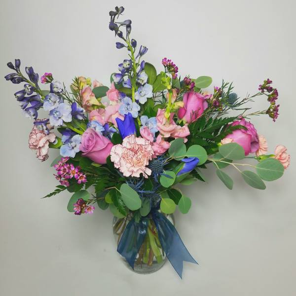 Mixed bouquet of pink and blue flowers in a glass vase with a blue ribbon