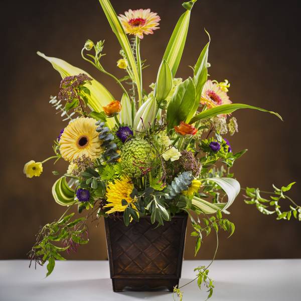 Tall mixed flower arrangement in a dark square vase