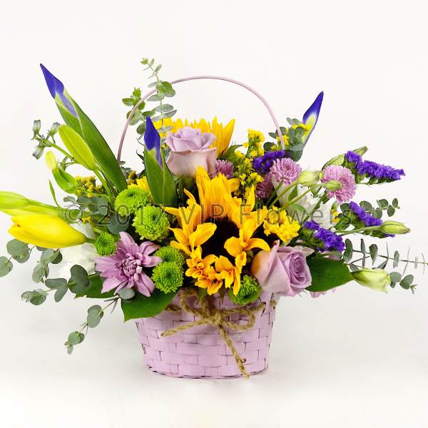 Mixed bouquet in a pink basket with yellow, purple, and lavender flowers