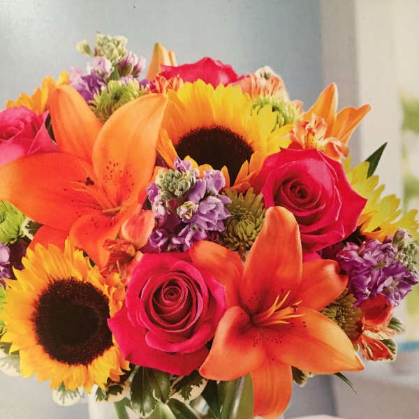 Bright mixed bouquet of sunflowers, roses, and lilies in a glass vase