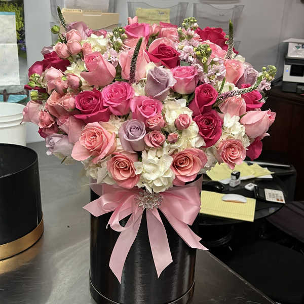 Pink and white rose arrangement in a black hatbox with a pink ribbon