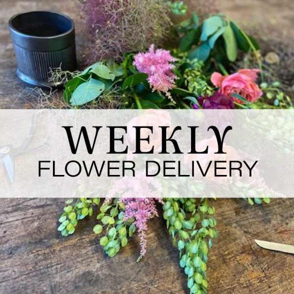 Loose floral arrangement with pink blooms and greenery beside a black container