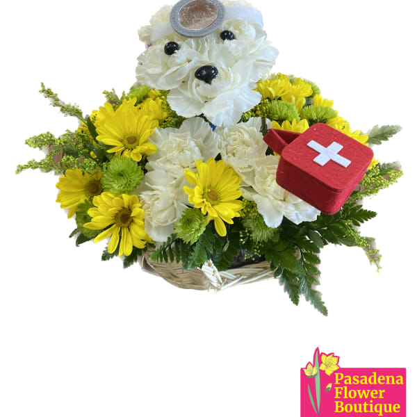 Basket arrangement with white flowers, yellow daisies, and a teddy bear holding a first-aid kit