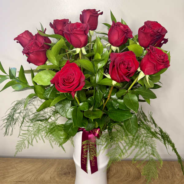 Red roses arranged in a white vase with trailing greenery.