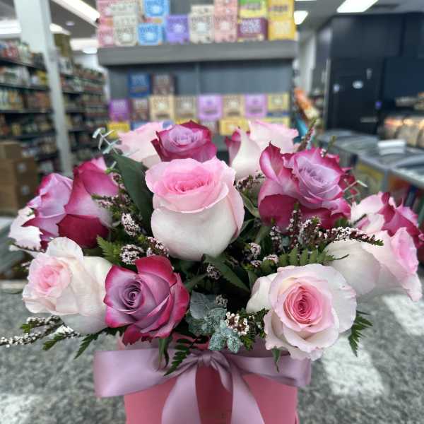 Pink and white roses arranged in a pink hat box with a ribbon.