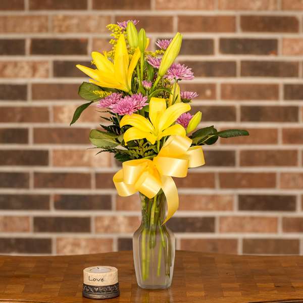 Yellow lilies and pink flowers in a glass vase with a yellow ribbon