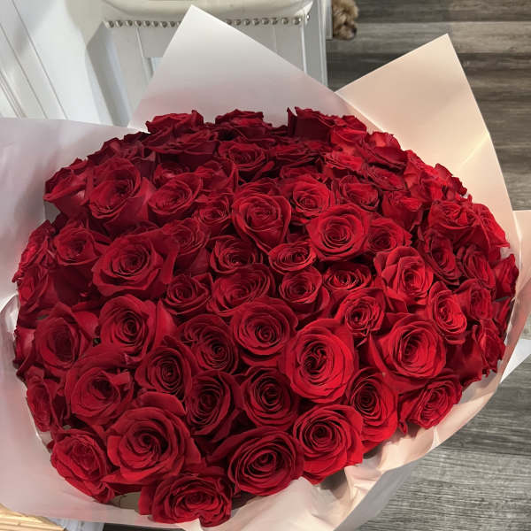 Large round bouquet of tightly packed red roses wrapped in white paper