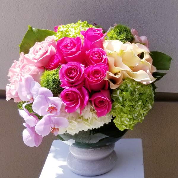 Pink roses and orchids arranged in a round vase centerpiece