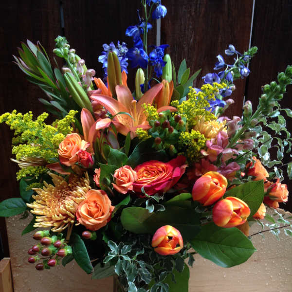 Mixed bouquet of orange, blue, and yellow flowers in a glass vase