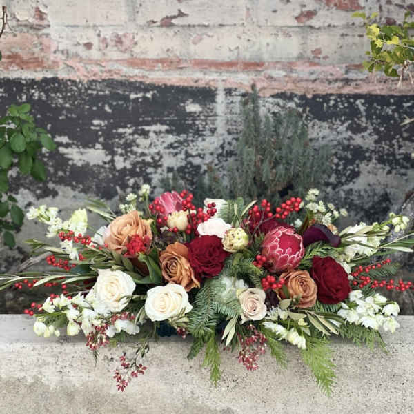 Low floral arrangement with roses, protea, and red berries